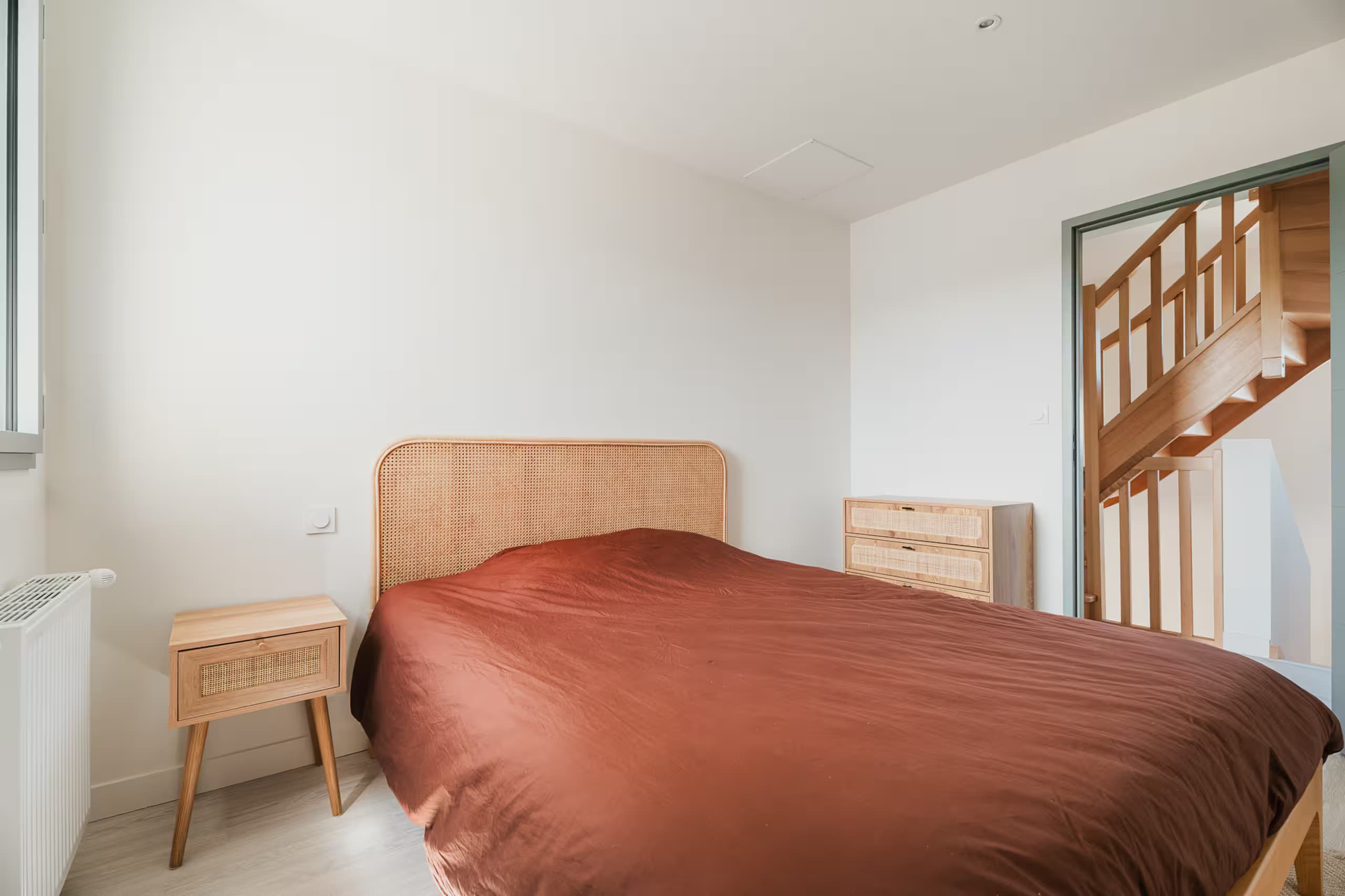 Chambre avec tête de lit en cannage et couverture terracotta