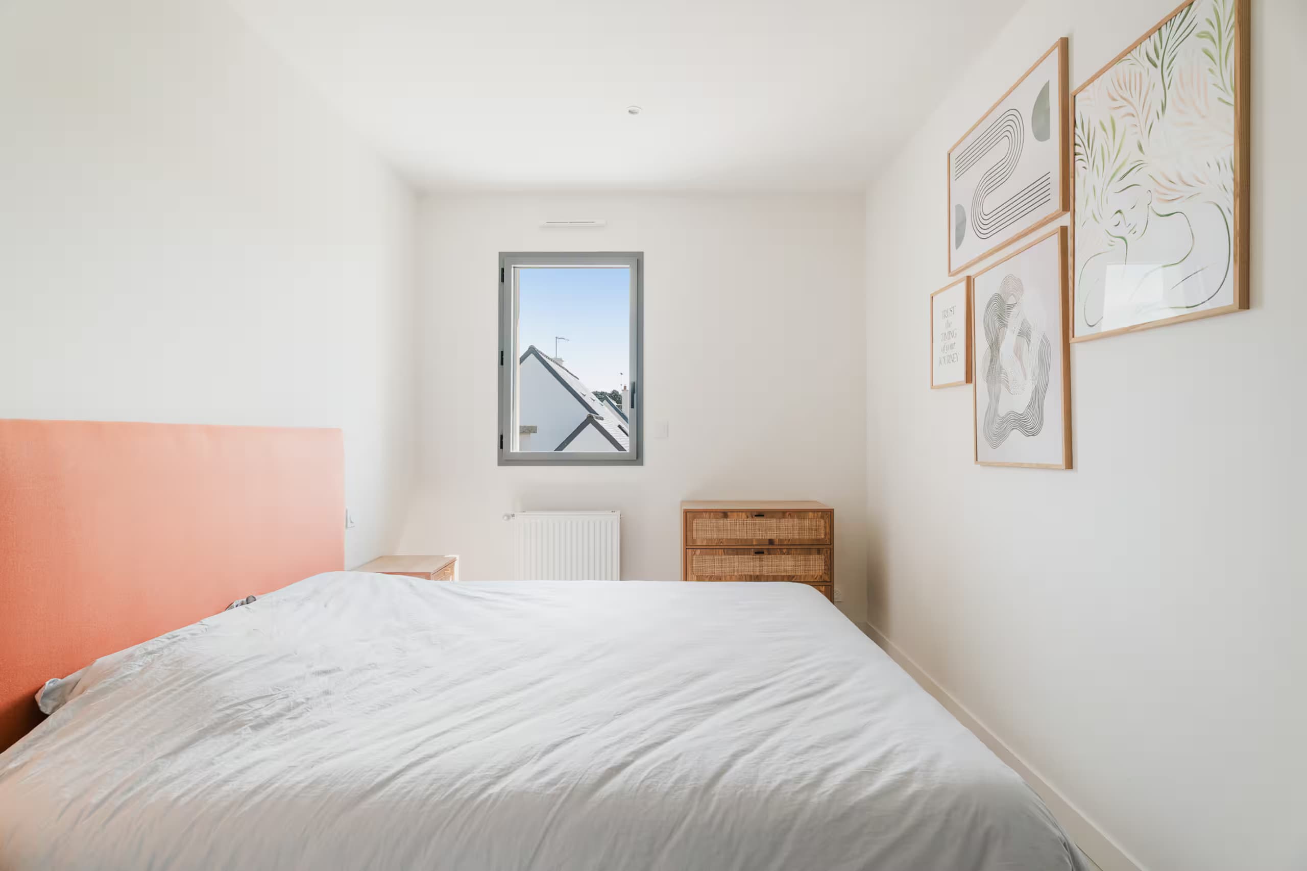 Chambre claire avec tête de lit corail et cadres au mur