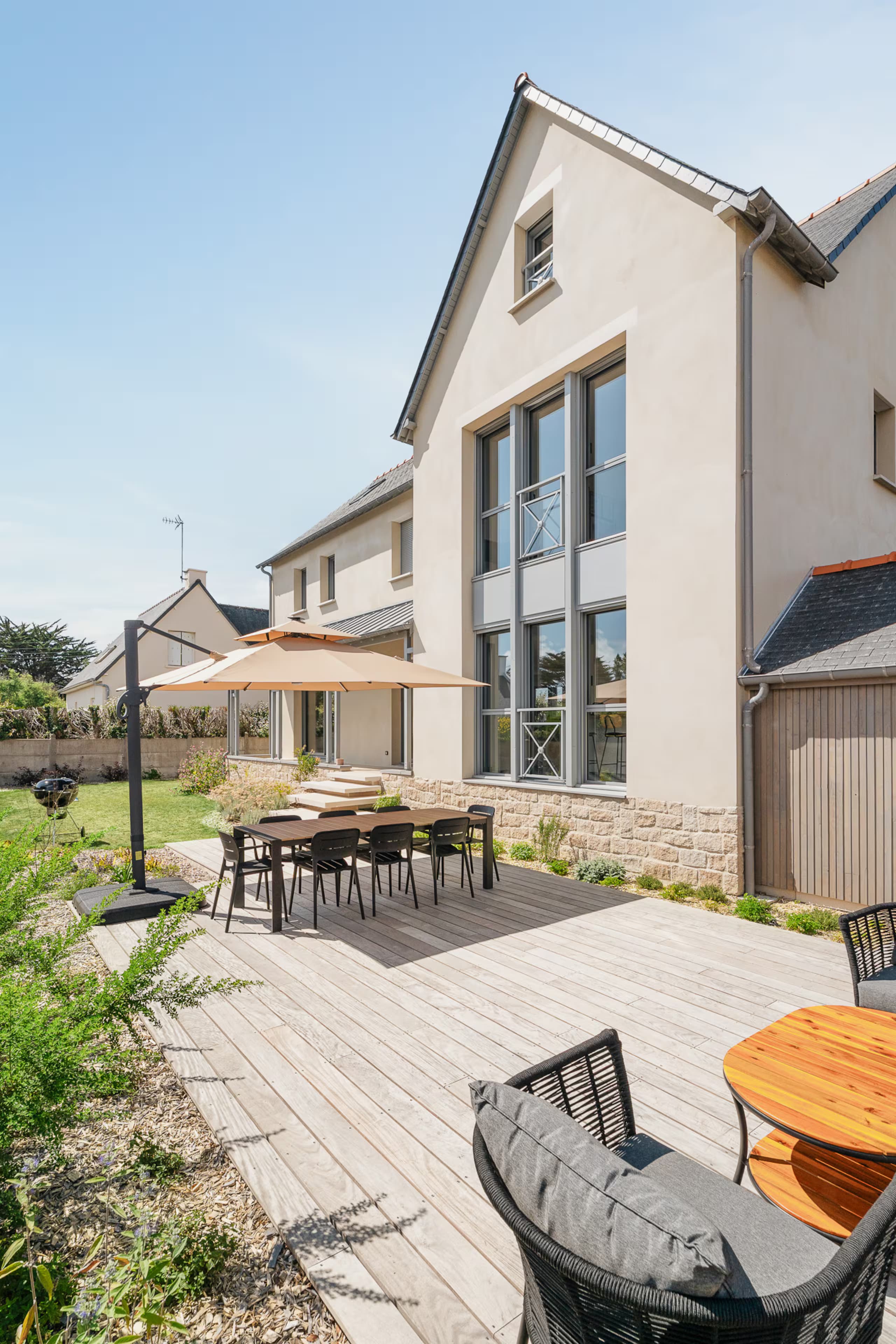 Grande terrasse en bois avec table, parasol et salon de jardin