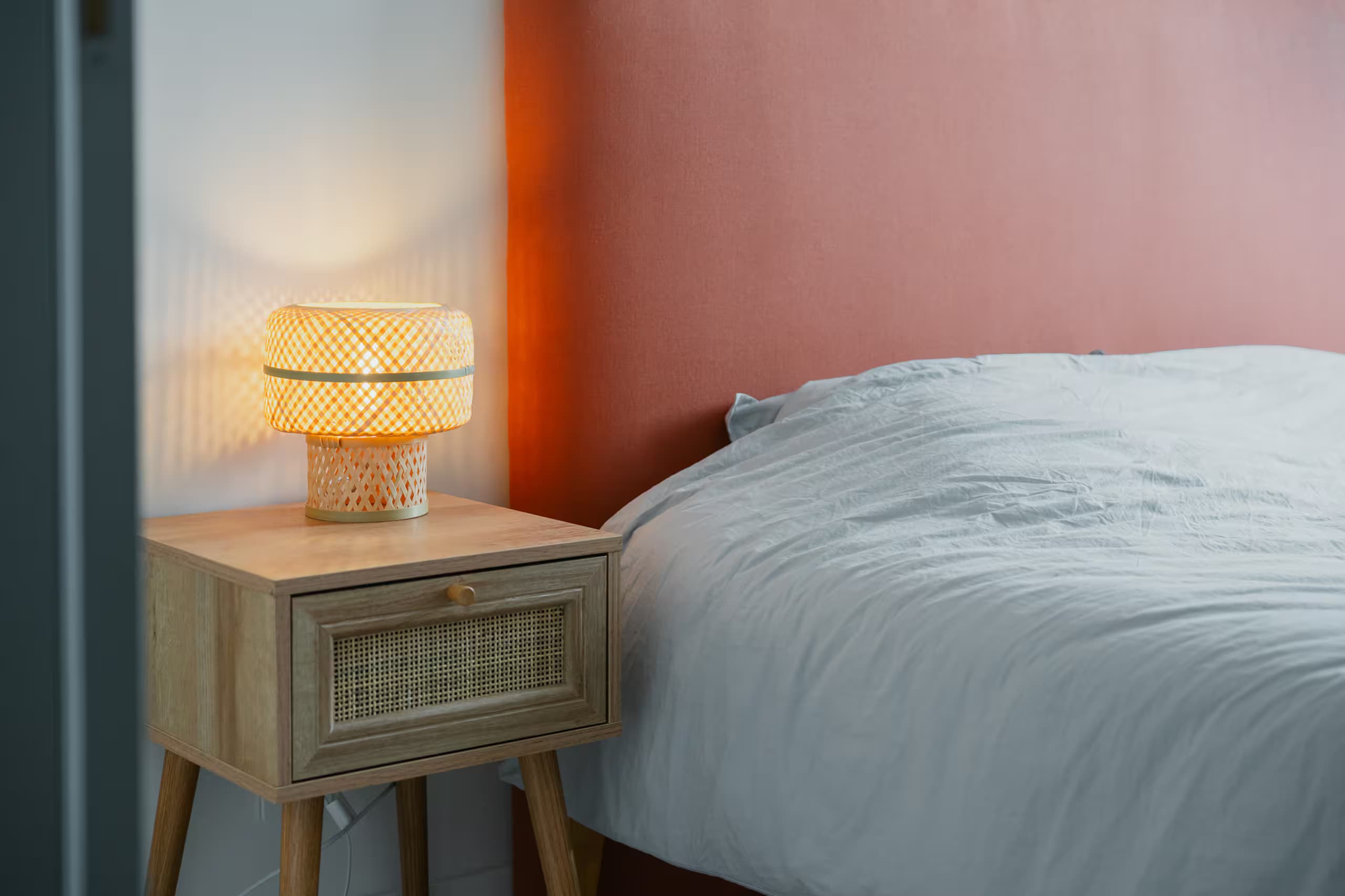 Table de chevet en cannage et lampe allumée